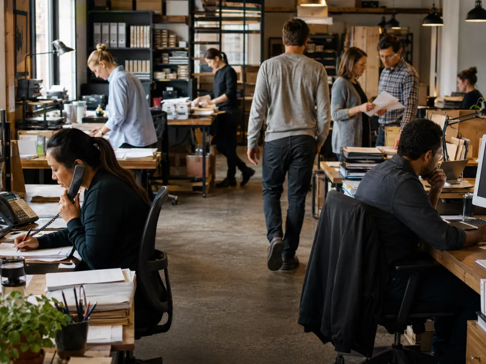 A busy office mid-shift with staff on calls, paperwork and people moving between desks
